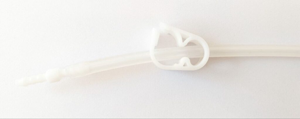 A transparent silicone hose with a white plastic clamp to restrict the flow in the tube.